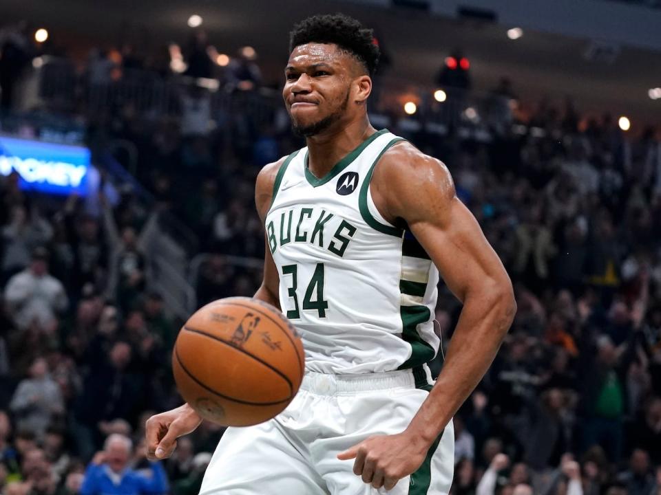 Giannis Antetokounmpo flexes after a dunk as the ball bounces past him during a game.