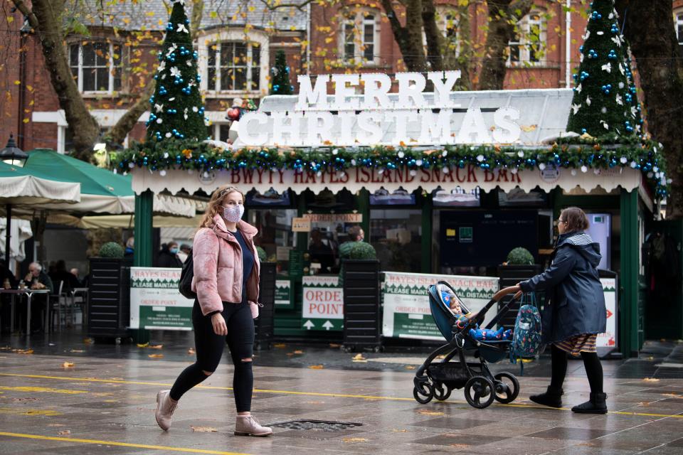 <p>A woman wearing a face mask walks past a cafe with a 'Happy Christmas' sign on The Hayes in Cardiff, Wales</p>Getty Images