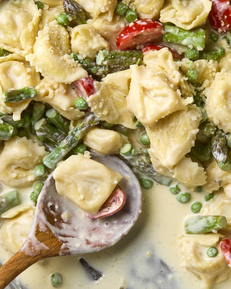 overhead shot of creamy tortellini primavera in a pan with some missing.