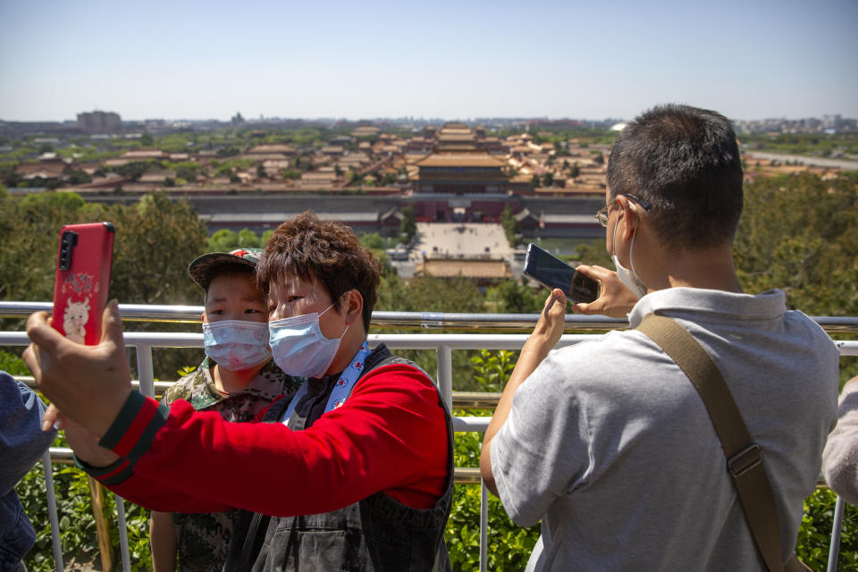 Visitors wearing face masks pose for a selfie at a viewing area overlooking the Forbidden City at a public park in Beijing, Saturday, May 1, 2021. Chinese tourists are expected to make a total of 18.3 million railway passenger trips on the first day of the country's five-day holiday for international labor day, according to an estimate by the state railway group, as tourists rush to travel domestically after the coronavirus has been brought under control in China. (AP Photo/Mark Schiefelbein)