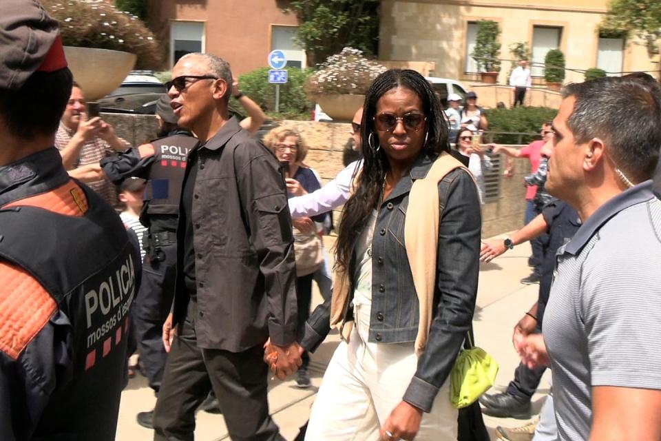 barack and michelle obama holding hands while walking through a crowd of people