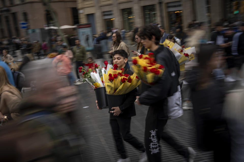 Vendors carry long stem roses along the historic La Rambla promenade as Catalans celebrate the day of their patron Saint Jordi, in Barcelona, Spain, April 23, 2024. (AP Photo/Emilio Morenatti)