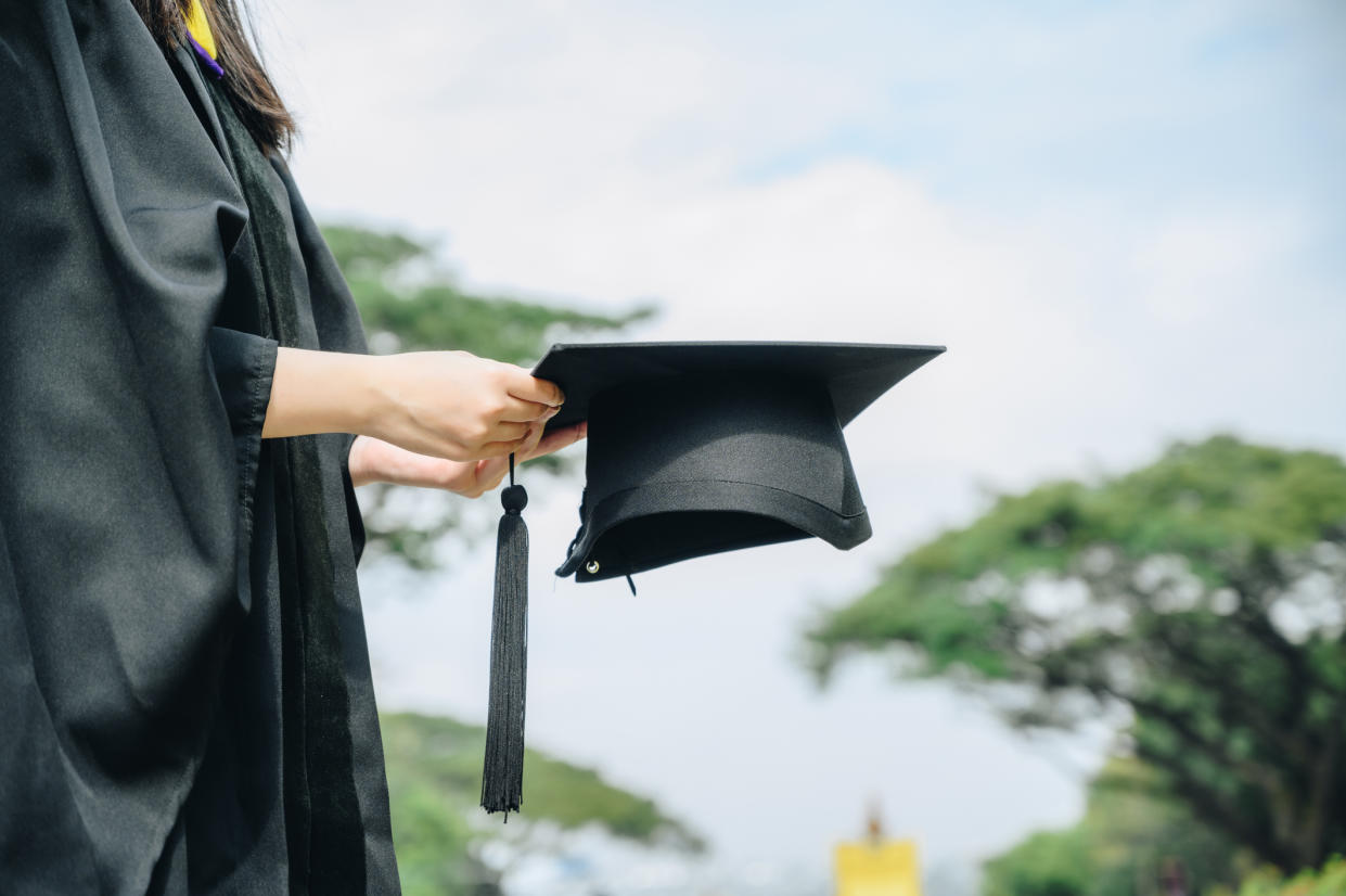 Student wearing graduation gown and holding a graduation cap.