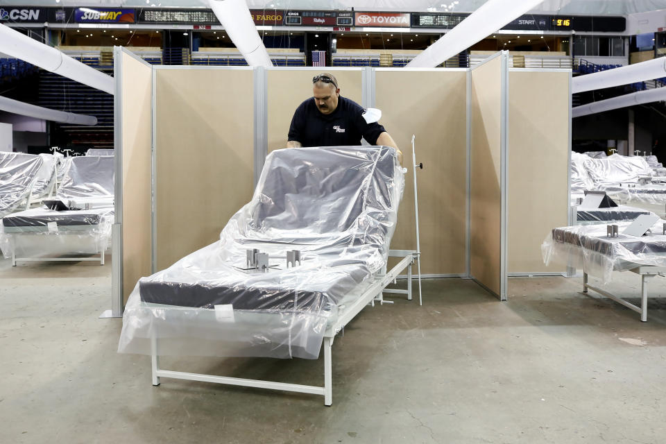 FILE - In this April 18, 2020, file photo Robert Reynolds, of the California Department of Forestry and Fire Protection, moves a bed into position as work is performed to turn Sleep Train Arena into a 400-bed emergency field hospital to help deal with the coronavirus outbreak, in Sacramento, Calif. Due to the recent spike in COVID-19 cases officials are rushing to reopen the former home of the NBA's Sacramento Kings, to patients. (AP Photo/Rich Pedroncelli, File)