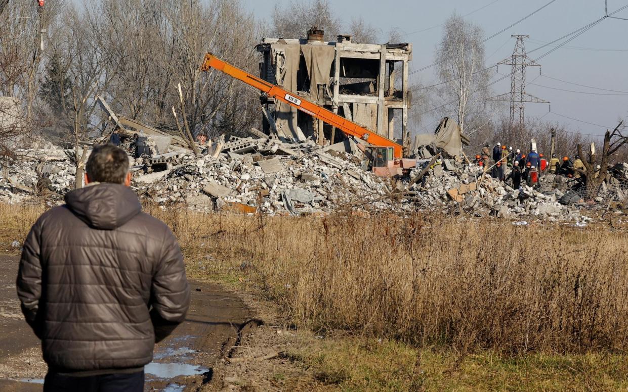 A man watches workers removing debris of a destroyed building purported to be a vocational college used as temporary accommodation for Russian soldiers, 63 of whom were killed in a Ukrainian missile strike - ALEXANDER ERMOCHENKO/ REUTERS