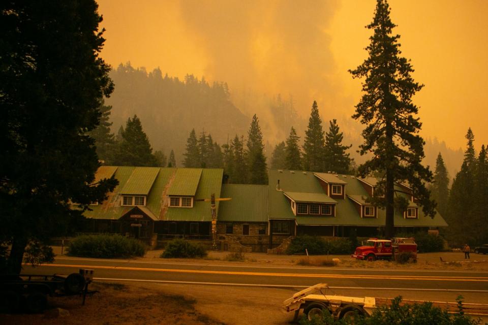 Smoke and a fire are seen behind a lodge near trees