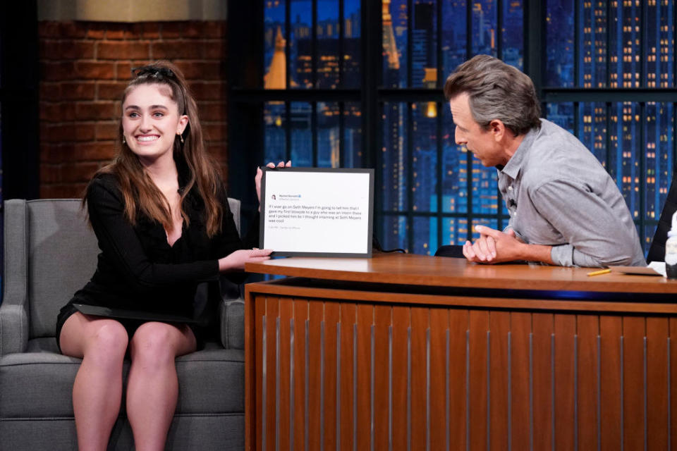 Rachel smiling and holding a framed copy of the tweet on Seth Meyers' show
