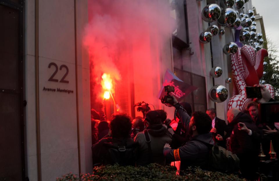 A group of protesters with flares and recording equipment pushing their way into LVMH's headquarters.