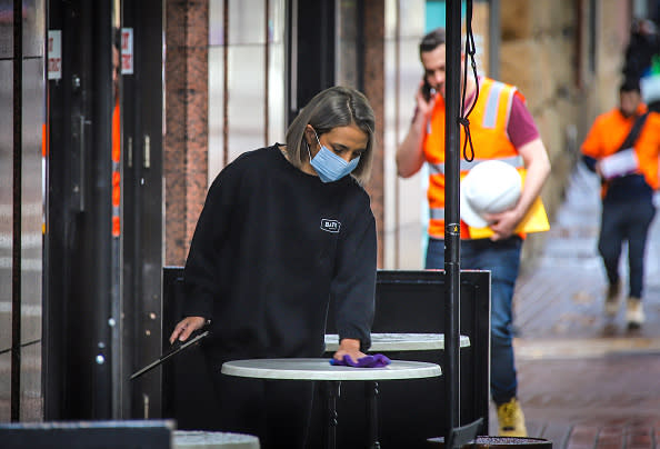 A worker wearing a face mask cleans a table for customers in Sydney, Australia. 