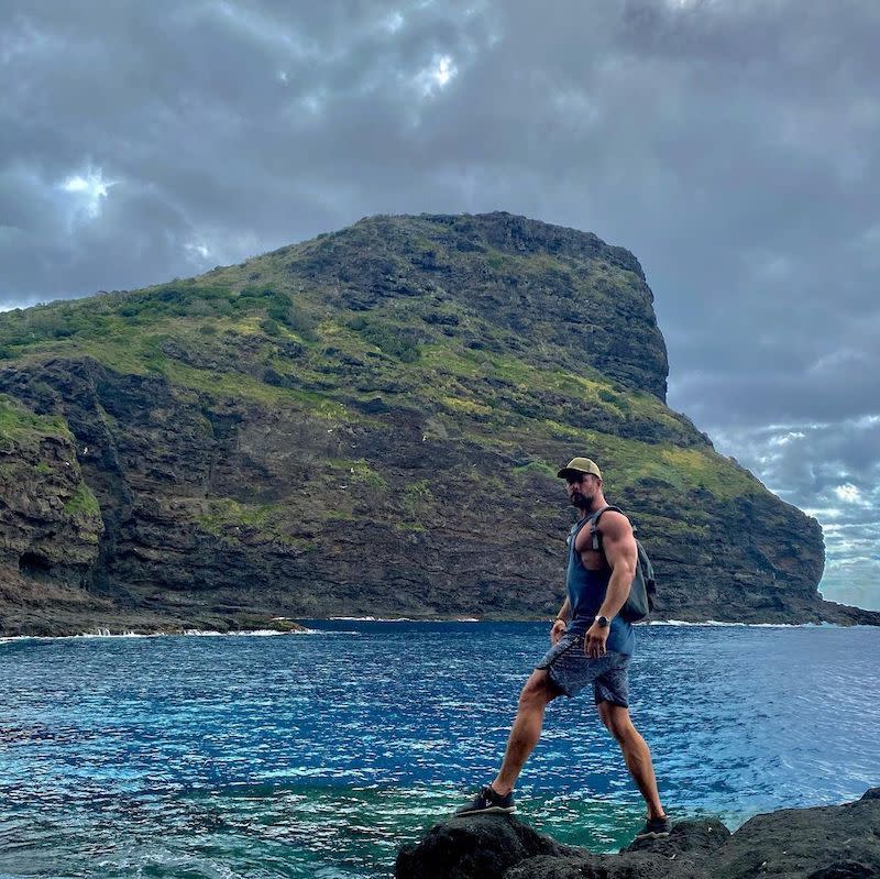 a man standing on a rock by a body of water with a mountain in the background