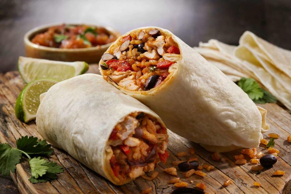 <p>Getty</p> A stock photo of a chicken burrito with black beans, roasted peppers, and cilantro