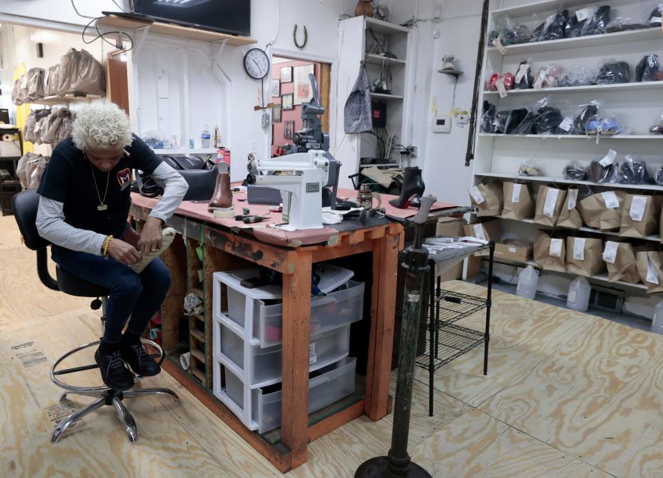 Ronda Morrison of the House of Morrison Shoe Repair on Livernois in Detroit works at adding masking tape to the side of the soles of boots before adding shoe polish to them inside her store on the Avenue of Fashion on Saturday, Nov. 18, 2023.