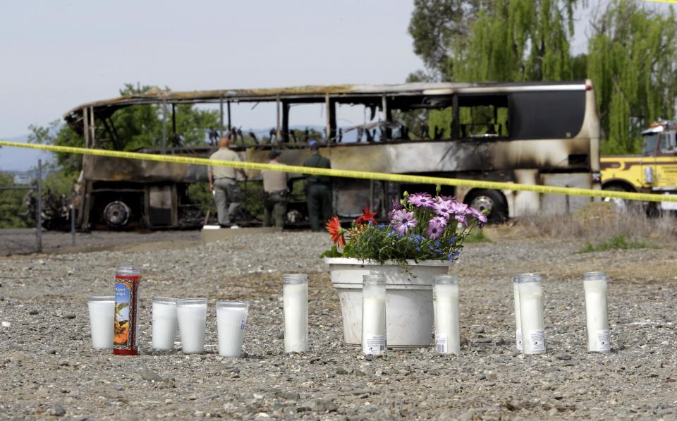 Candles and flowers are seen at a make-shift memorial, Friday, April 11, 2014, for the victims of a multi-vehicle accident that included a tour bus and a FedEX truck crashed on Interstate 5 in Orland, Calif. Ten people were killed and dozens injured in the fiery crash, Thursday, between the truck and a bus seen in background, carrying high school students on a visit to a Northern California College.(AP Photo/Rich Pedroncelli)