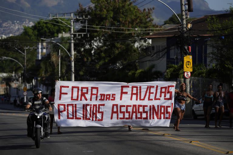 Los residentes caminan sosteniendo una pancarta con un mensaje que dice en portugués: "Fuera de la policía asesina de la favela", después de una operación policial que resultó en múltiples muertes, en la favela Complexo do Alemao en Río de Janeiro, Brasil, el jueves 21 de julio de 2022. 