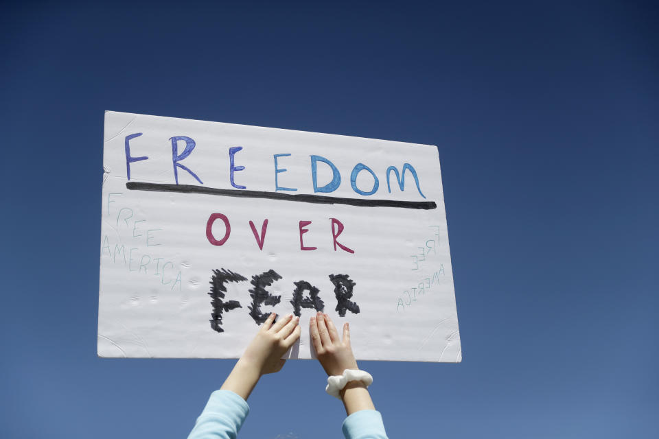 FILE - In this April 21, 2020, file photo a person holds a sign while gathering with others to protest stay-at-home orders put into place due to the COVID-19 outbreak outside the Missouri Capitol in Jefferson City, Mo. Amid pockets of attention-grabbing protests, a new survey finds Americans remain overwhelming in favor of stay-at-home orders and other efforts to slow the spread of coronavirus. (AP Photo/Jeff Roberson, File)