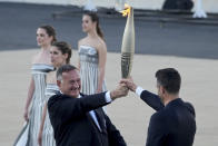 Tony Estanguet, President of Paris 2024, right, receives the Olympic flame from Spyros Capralos, head of Greece's Olympic Committee, during the flame handover ceremony at Panathenaic stadium, where the first modern games were held in 1896, in Athens, Friday, April 26, 2024. On Saturday the flame will board the Belem, a French three-masted sailing ship, built in 1896, to be transported to France. (AP Photo/Petros Giannakouris)