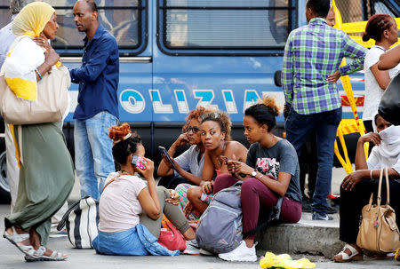 Refugees sit on a kerb next to a police van, after being forcibly removed from a building where they had been living, in central Rome, Italy, August 20, 2017. REUTERS/Alessandro Bianchi