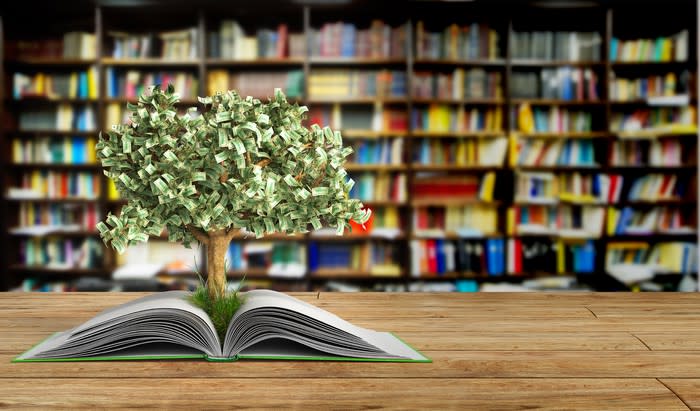 A tree with money for leaves growing out of an open book in a library.