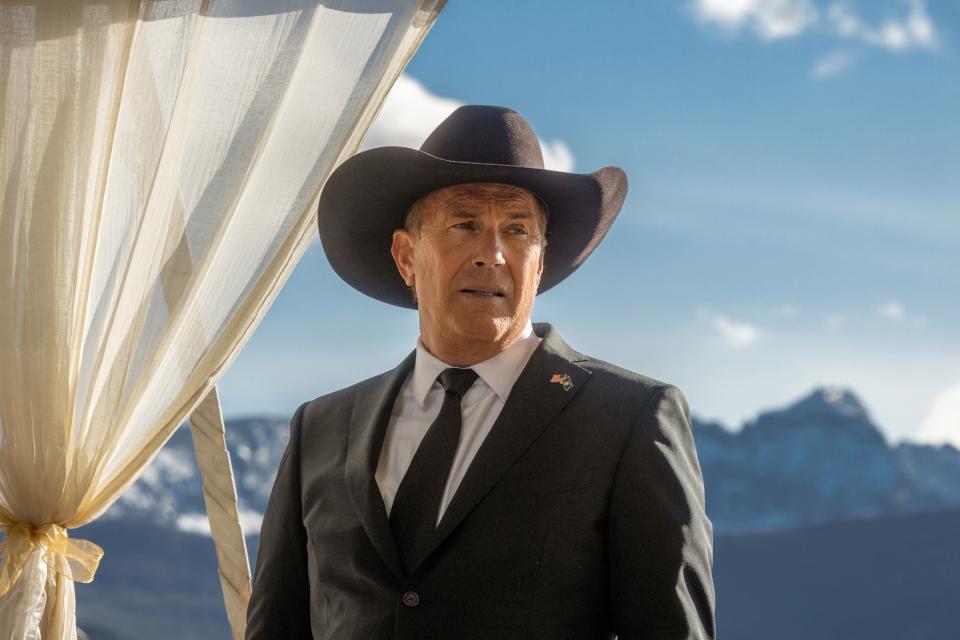 Kevin Costner in character as John Dutton from "Yellowstone," wearing a suit and cowboy hat with mountains in the background