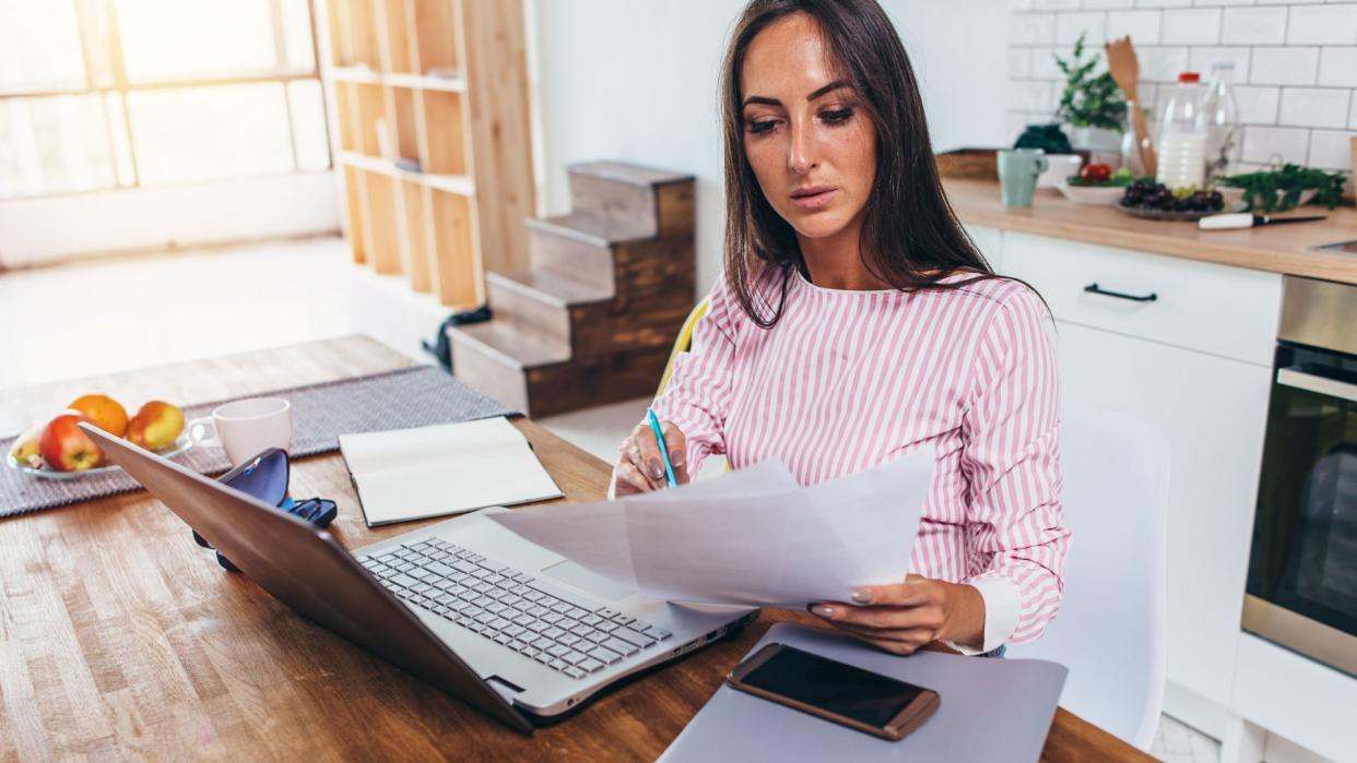 Woman working with documents and laptop in the kitchen at home.