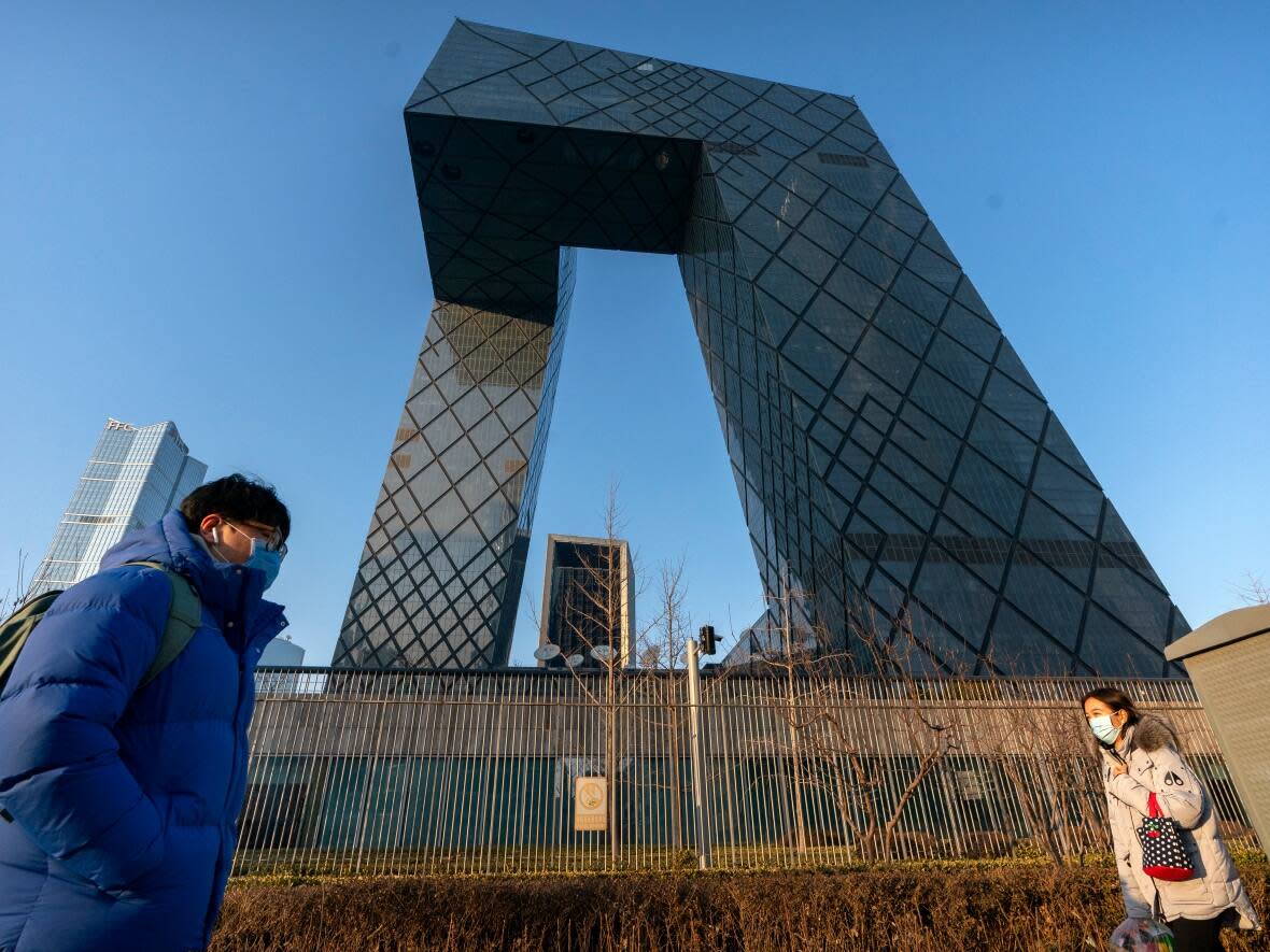 People walk past the CCTV headquarters building, the home of Chinese state-run television network CCTV and its overseas arm CGTN, in Beijing on Feb. 4, 2021. (Mark Schiefelbein/The Associated Press - image credit)