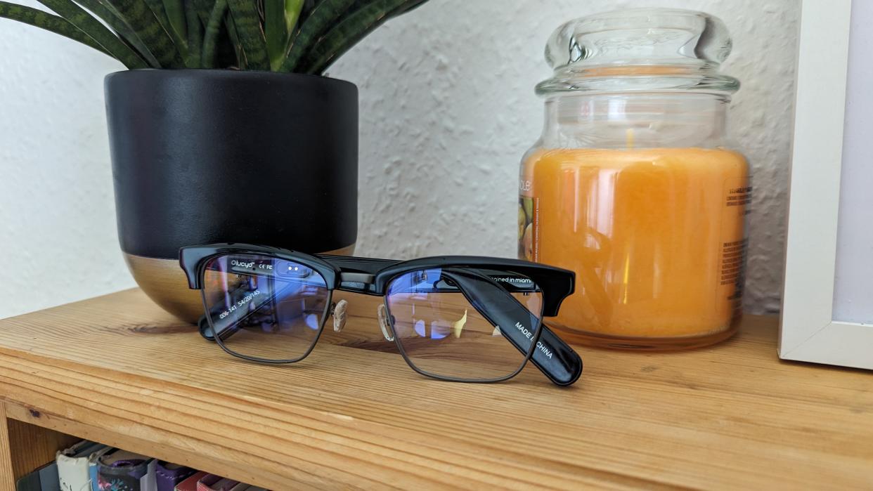  The Lucyd Lyte glasses next to a plant and a yellow candle sat on a bookshelf. 