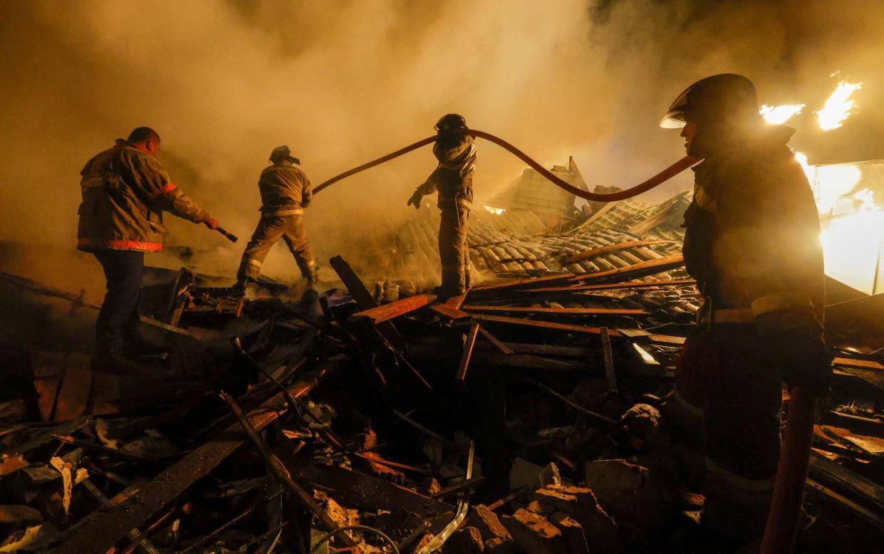 A team of firefighters scramble over the debris of a destroyed building as a fire blazes behind them - REUTERS/Alexander Ermochenko