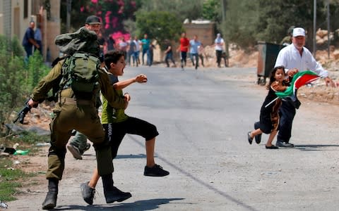An Israeli soldier temporarily detains a Palestinian youth during clashes following a weekly protest against the expropriation of Palestinian land by Israel, in the village of Kfar Qaddum - Credit: JAAFAR ASHTIYEH/AFP/Getty Images