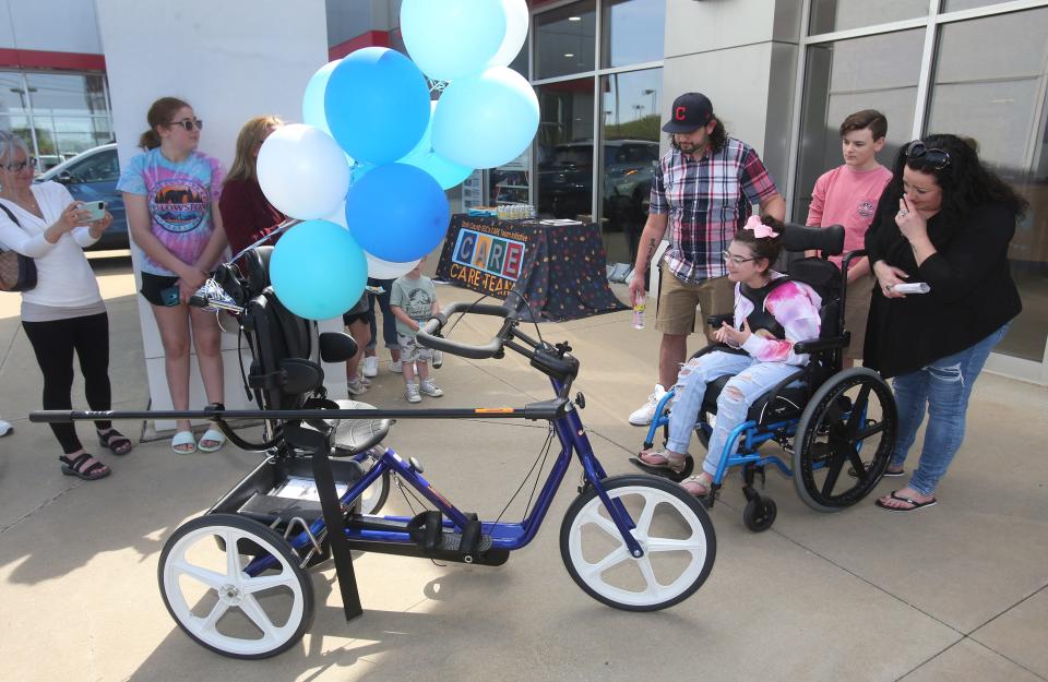 Miah McClure gets a first look at her new adaptive tricycle that was presented this week to the Hoover High student at Cain Toyota-BMW in Jackson Township. With her, from left, are her father, Sam, younger brother, Joey, and her mother, Bre.