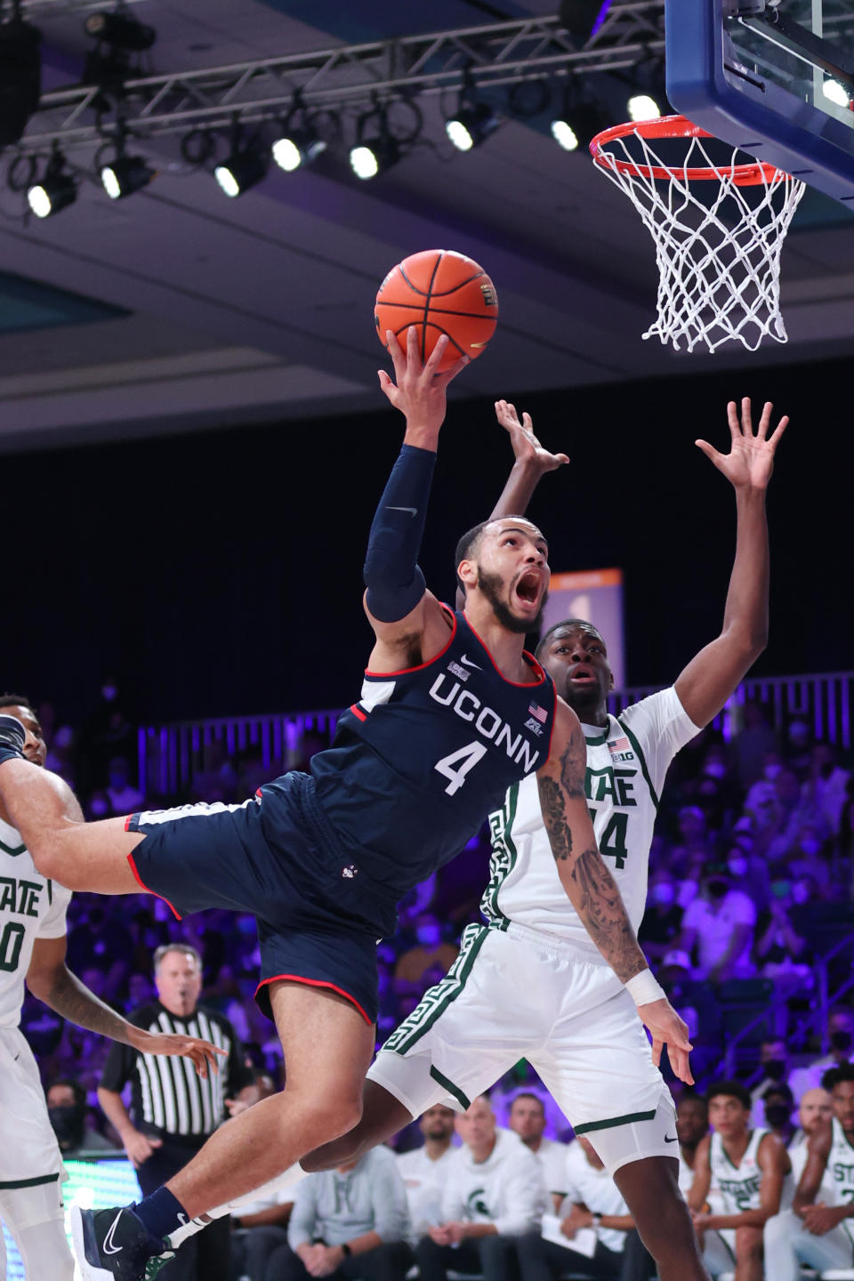 In this photo provided by Bahamas Visual Services, Connecticut guard Tyrese Martin (4) goes to the basket as Michigan State forward Gabe Brown (44) defends during an NCAA college basketball game at Paradise Island, Bahamas, Thursday, Nov. 25, 2021. (Tim Aylen/Bahamas Visual Services via AP)