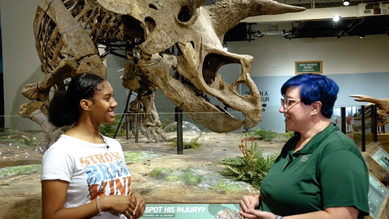  A student host discusses the Triceratops Skeleton behind her.  