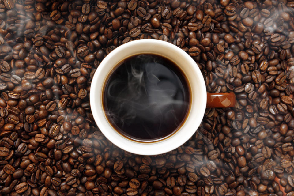 Cup of black coffee overhead view, on top of a pile of raw coffee beans