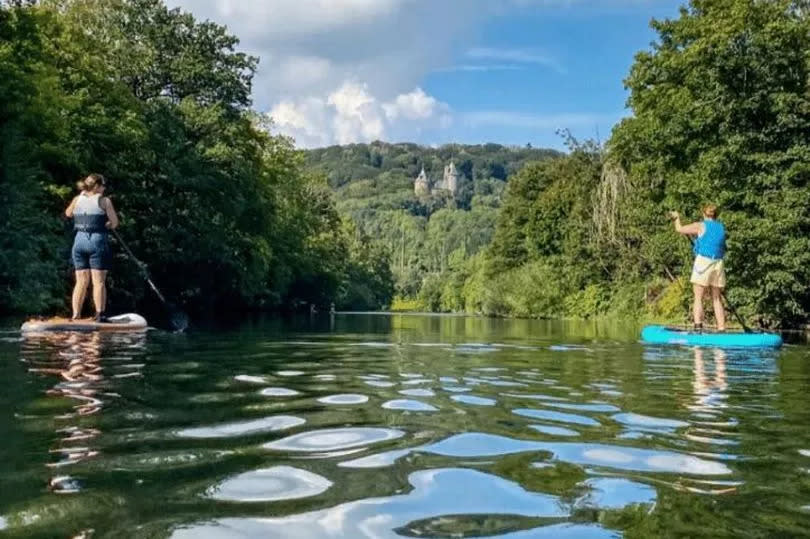 Two paddleboarders on the river Taff with Castell Coch in view