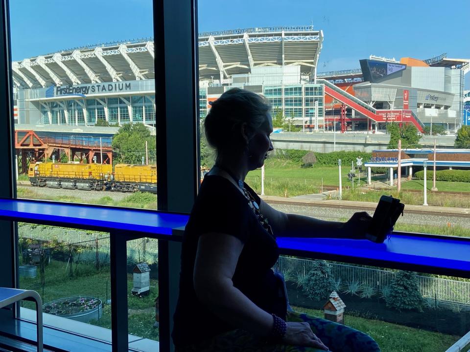 Retired firefighter Michelle Krause checks her phone during a break at the American Massage Therapist Association national convention at the Huntington Convention Center in Cleveland, Ohio, Thursday, Aug. 25, 2022. In the background is FirstEnergy Stadium, home of the Cleveland Browns NFL football team. (AP Photo/Teresa Walker)