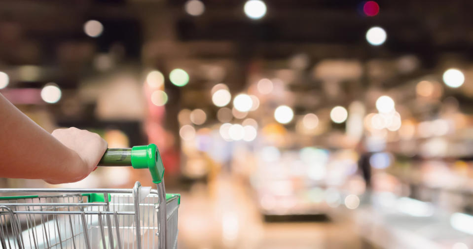 woman hand hold supermarket shopping cart with Abstract grocery store shelves blurred defocused background with bokeh light