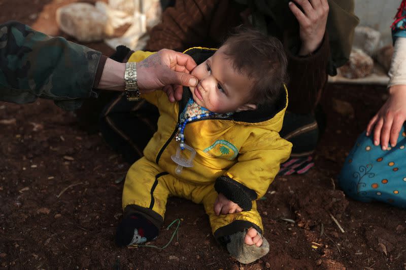 An internally displaced man pinches the cheek of a child wearing socks with a hole at a makeshift camp in Azaz