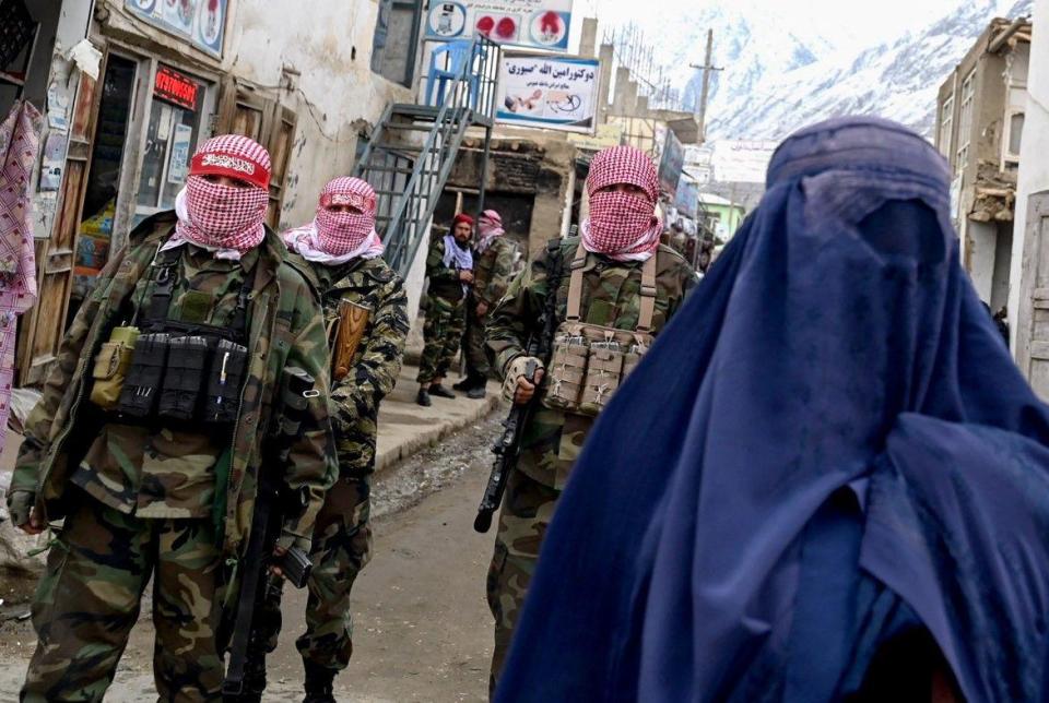 Taliban security personnel stand guard as an Afghan burqa-clad woman (R) walks along a street at a market in the Baharak district of Badakhshan province on February 26, 2024