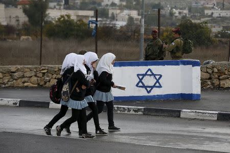 Palestinian school girls walk past Israeli soldiers at a checkpoint at a entrance to the village of Beit Einun near the West Bank city of Hebron December 1, 2015. REUTERS/Baz Ratner