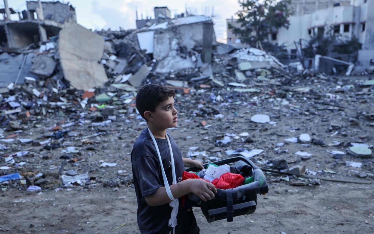 A Palestinian boy carries salvageable items amid the rubble of buildings destroyed during Israeli airstrikes in the Rafah refugee camp in the southern of Gaza Strip, on October 16, 2023