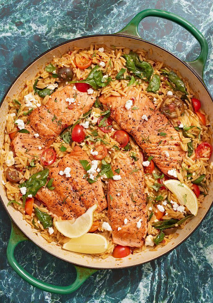 salmon and orzo with baby tomatoes, feta, baby spinach, and lemon wedges in a green dutch oven