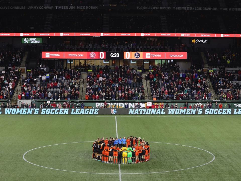 NWSL players from the Portland Thorns and Houston Dash pause their game and huddle in the center circle to protest the league and honor survivors of sexual abuse at the hands of a former coach.