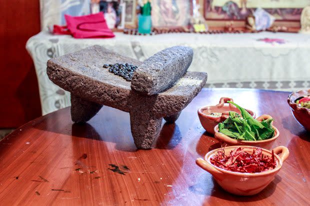 En la casa de Romero Contreras en San Lucas Xochimanca, frijoles negros esperan ser triturados en un metate, un tipo de mortero hecho de roca volcánica tallada. En las cazuelas más abajo, chiles (al frente), epazote y los frijoles triturados están listos para ser cocinados. Foto: Mayela Sánchez, GPJ Mexico. prehispánicos