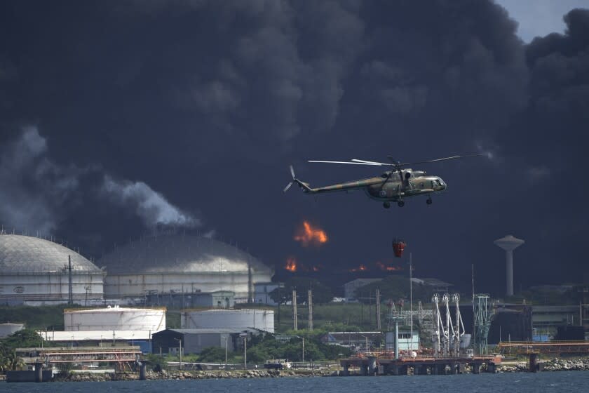 A helicopter carrying water flies over the Matanzas Supertanker Base, as firefighters try to quell the blaze which began during a thunderstorm the night before, in Matazanas, Cuba, Saturday, Aug. 6, 2022. Cuban authorities say lightning struck a crude oil storage tank at the base, causing a fire that led to four explosions which injured more than 50 people. (AP Photo/Ramon Espinosa)