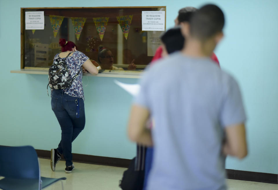 A woman fills out a form at a receiving window as others wait their turn at the Department of Family Affairs, in Bayamon, Puerto Rico, Friday, March 29, 2019. Hundreds of thousands of Puerto Ricans are feeling the sting of what the territorial government says are insufficient federal funds to help the island recover from the Category 4 storm amid a 12-year recession. (AP Photo/Carlos Giusti)