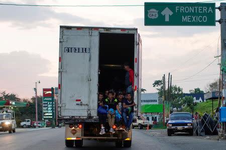 Immigrants pass by a highway sign that reads in Spanish: "Mexico Border", as they take a lift in the back of a truck during their journey towards the United States, in Pajapita, Guatemala, January 17, 2019. REUTERS/Alexandre Meneghini