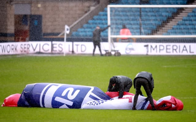 Staff struggle to hold on to a centre circle cover during high winds ahead of Millwall v West Brom