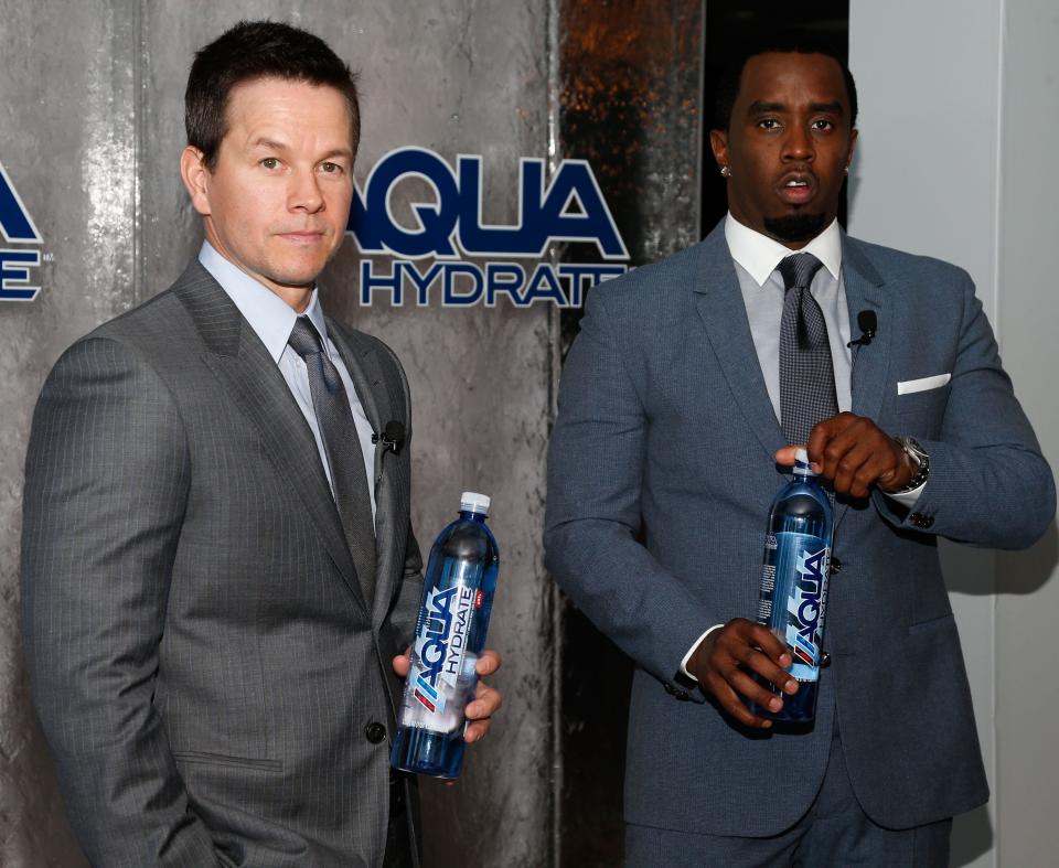 Mark Wahlberg and Sean Combs in suits holding water bottles