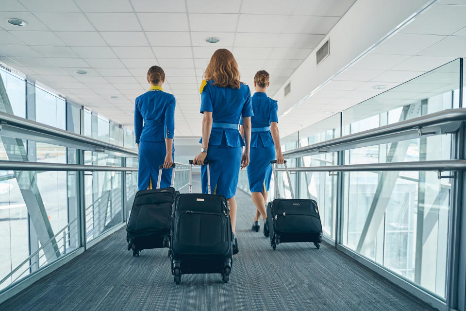 Three flight attendants with luggage walking through an airport walkway