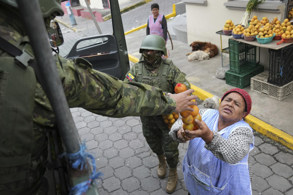 A fruit vender gifts oranges to soldiers patrolling a residential area on the south side of Quito, Ecuador, Friday, Jan. 12, 2024, in the wake of the apparent escape of a powerful gang leader from prison. President Daniel Noboa decreed Monday a national state of emergency, a measure that lets authorities suspend people’s rights and mobilize the military. (AP Photo/Dolores Ochoa)