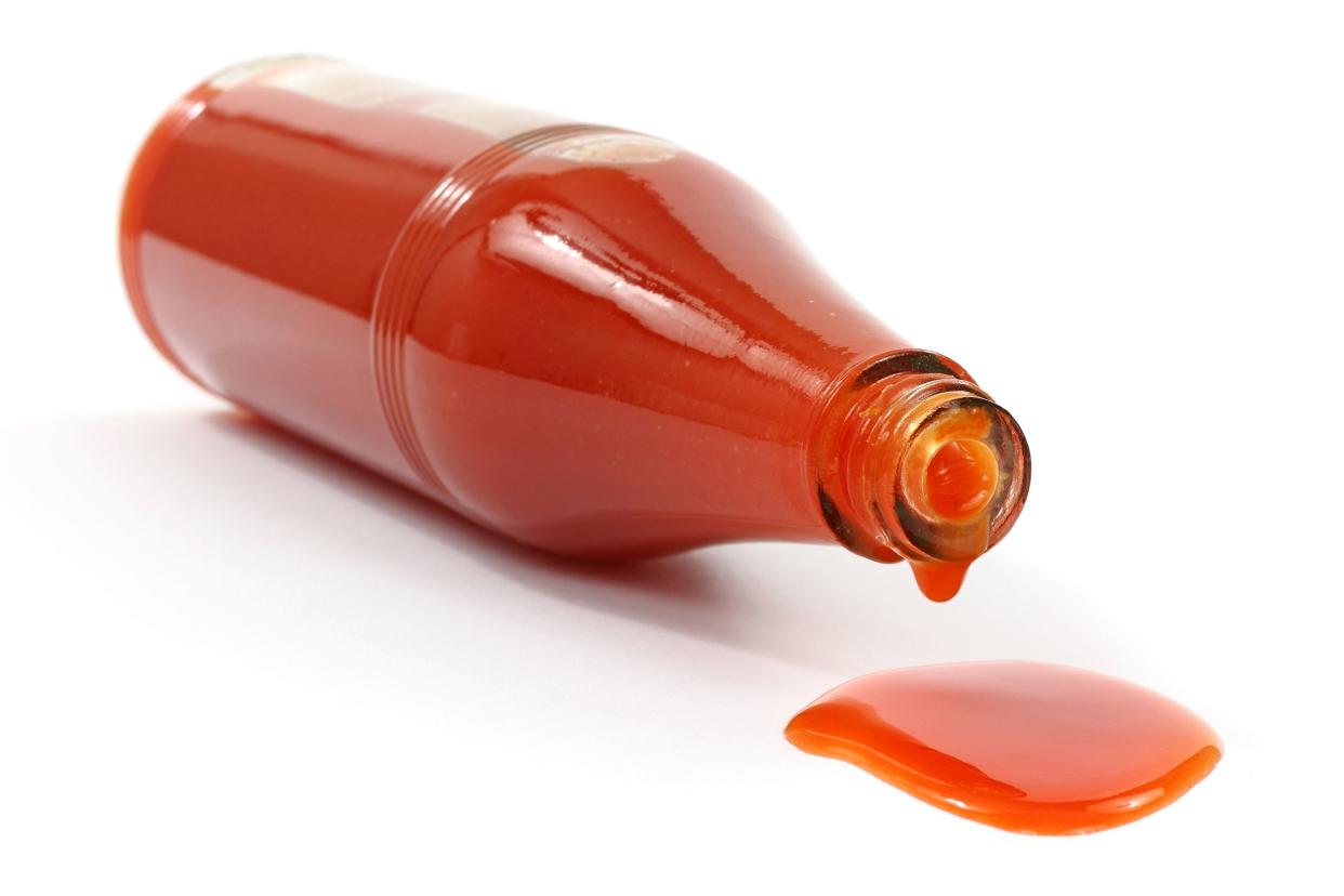 Hot sauce spilling from a glass bottle lying on a white surface